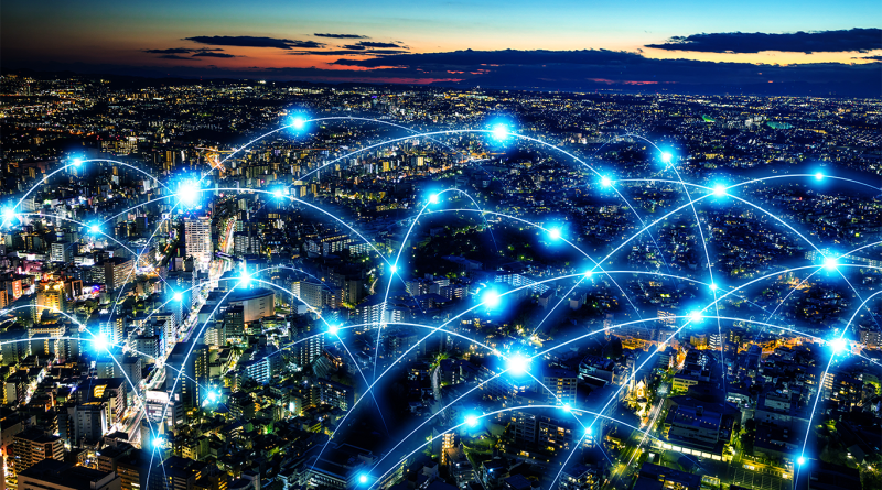 Digital image of a birds-eye view shot of a city with blue holographic lines connecting to each building to support 5G Manufacturing article