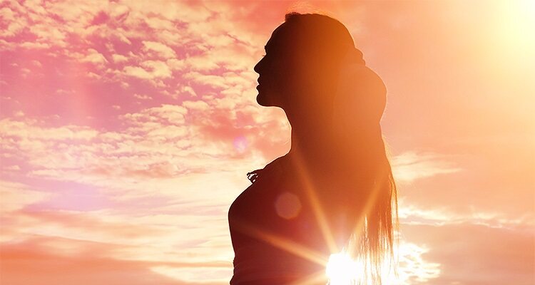 silhouette of a woman in a long dress standing in front of the sun