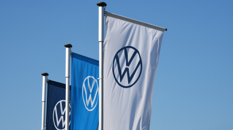 Volkswagen flags outside OEM facility under blue sky, representing original equipment manufacturer leadership and original parts production.