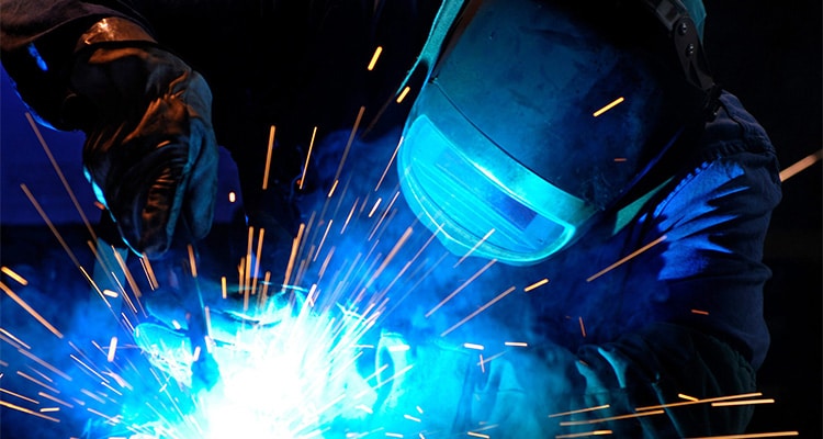 Person wearing welding mask welds metal in a factory close up