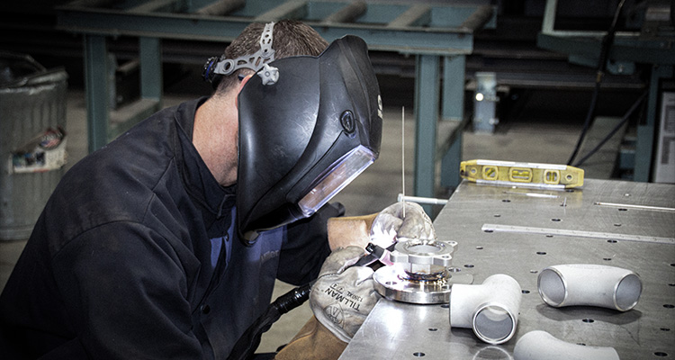 a person performing TIG (Tungsten Inert Gas) welding on a metal workbench