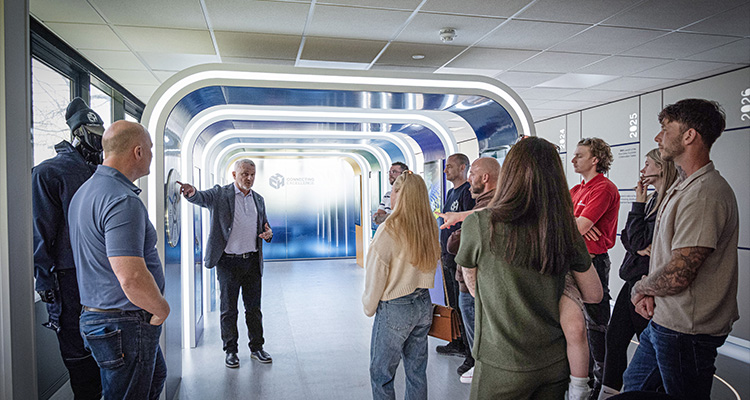 a man speaking to a group of people in a modern hallway with a futuristic design