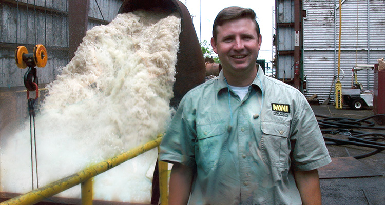 an MWI employee standing next to a large pump discharging foamy water
