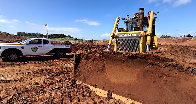 a construction site with a large yellow Komatsu bulldozer in the foreground, partially pushing a mound of reddish-brown dirt
