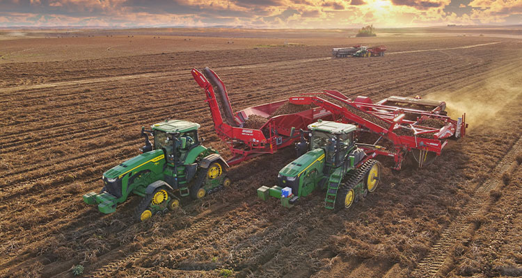 a Spudnik potato harvester being pulled by two John Deere tractors