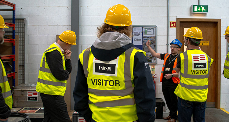 individuals wearing high-visibility "VISITOR" safety vests at an industrial or warehouse site