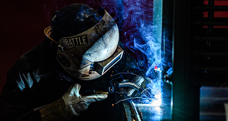 a welder, actively engaged in welding metal in a dimly lit industrial environment