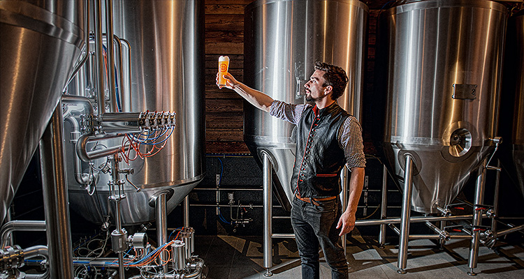 a man examining a glass of beer in a craft brewery setting.