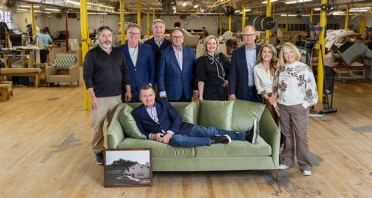 a group of people posing for a corporate photo within what appears to be a furniture manufacturing facility or workshop