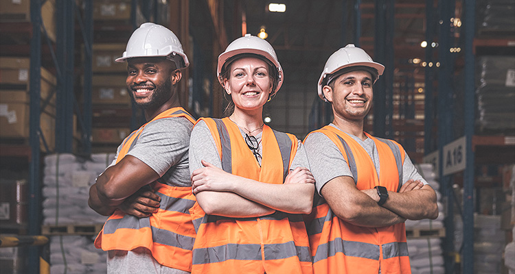 Three people in orange high visibility jackets in a warehouse