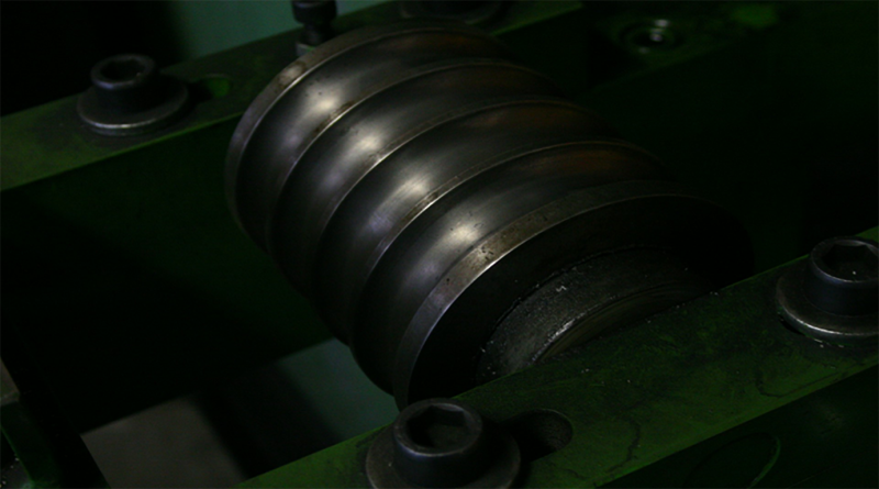 Close-up of a metal industrial spindle or roller assembly mounted in a green machine frame.
