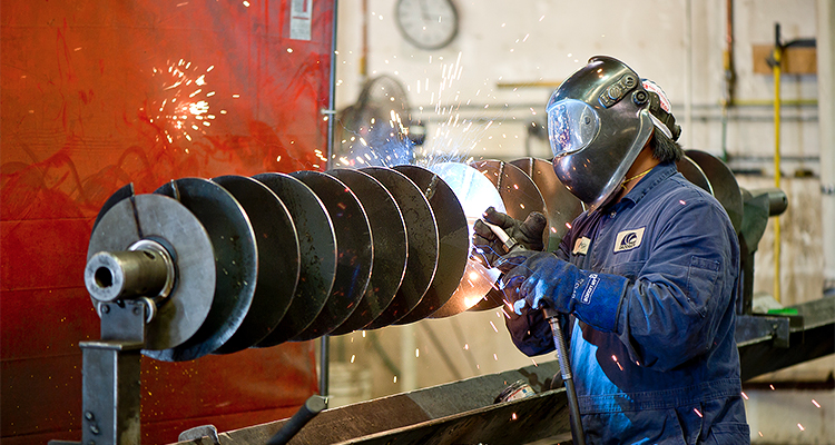 A legacy built on turning challenges into opportunity a worker performing industrial welding on a conveyor screw component.